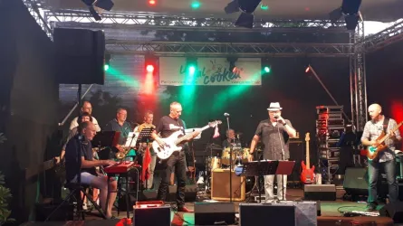 Eine Band spielt auf einer Bühne mit verschiedenen Instrumenten. Bunte Lichter beleuchten die Szene und schaffen eine festliche Atmosphäre.