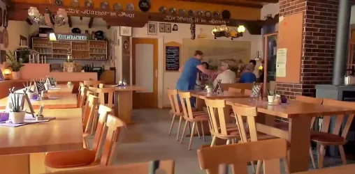 Ein gemütliches Restaurant mit Holztischen und Stühlen. Im Hintergrund sind Mitarbeiter mit Gästen beschäftigt.