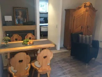 Ein gemütlicher Essbereich mit einem Holztisch und eleganten Stühlen. Im Hintergrund steht ein antik aussehender Schrank und ein Gemälde an der Wand.