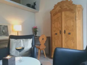 Ein gemütlicher Wohnraum mit einem eleganten Holzschrank und modernen Möbeln. Ein Glas Wein und eine Kerze sorgen für eine entspannte Atmosphäre.