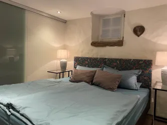 Ein gemütliches Schlafzimmer mit einem großen Bett und hellen Kissen. Zwei Nachttische und eine sanfte Beleuchtung sorgen für eine entspannte Atmosphäre.