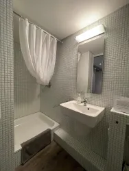 Ein modernes Badezimmer mit hellen Fliesen und einer Dusche. Es gibt ein Waschbecken und einen großen Spiegel.