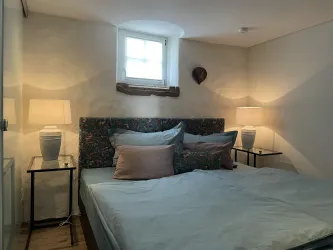 Ein gemütliches Schlafzimmer mit einem großen Bett und bunten Kissen. Die Wände sind hell und es gibt zwei Lampen auf Nachttischen.