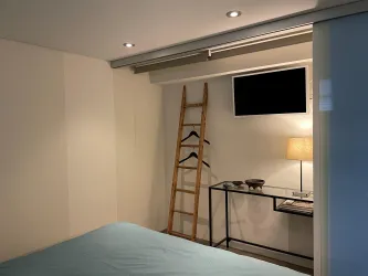 Ein modernes Schlafzimmer mit einem Bett und einer Holzleiter an der Wand. Neben dem Bett stehen ein Tisch mit Lampen und ein Fernseher an der Wand.
