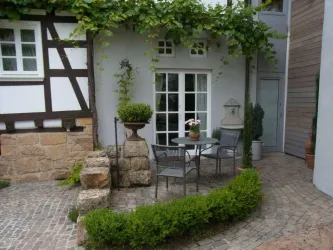 Ein schöner Außenbereich mit einem kleinen Tisch und Stühlen. Umgeben von Pflanzen und einem historischen Brunnenelement.