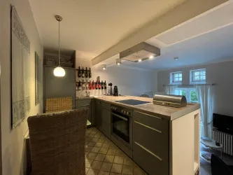 Eine moderne Küche mit einem Kochfeld und einem Essbereich. Regale mit Weinen sind im Hintergrund sichtbar.