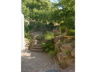 Ein gemütlicher Gartenweg mit Steinen und üppiger Vegetation. Die Atmosphäre ist ruhig und einladend.