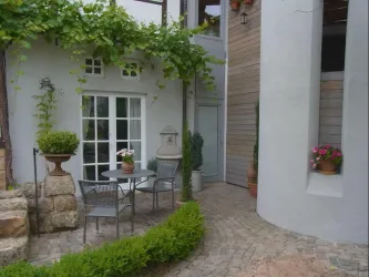 Ein gemütlicher Innenhof mit einem Tisch und Stühlen. Umgeben von Grünpflanzen und dekorativen Töpfen.