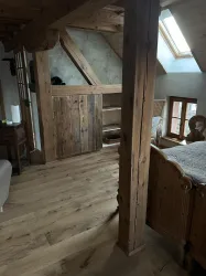 Ein gemütlicher Raum mit Holzverkleidung und einem Fenster, das Licht hereinlässt. Der Boden ist aus edlem Holz, und es gibt eine Verbindung zu einem weiteren Bereich.