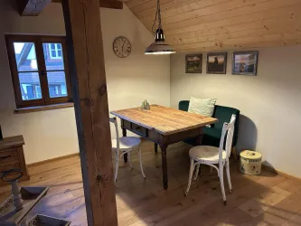 Ein gemütlicher Essbereich mit einem Holztisch und weißen Stühlen. Die Wände sind mit Bildern dekoriert, und der Raum hat große Fenster mit Blick nach draußen.