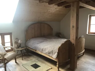 Ein gemütliches Schlafzimmer mit einem großen Holzbett und rustikalem Flair. Die Wände sind aus Holz, und es gibt einen kleinen Tisch sowie einen Stuhl.