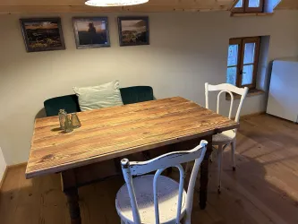 Ein gemütlicher Essbereich mit einem Holztisch und zwei Stühlen. An der Wand hängen Bilder und das Licht schafft eine einladende Atmosphäre.