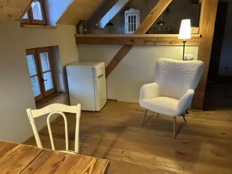 Ein gemütlicher Raum mit Holzfußboden und holzverzierten Wänden. Es gibt einen weißen Stuhl, einen Kühlschrank und eine Lampe, die eine warme Atmosphäre schafft.
