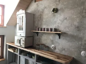Eine moderne Küche mit einem rustikalen Holzregal und einem alten Küchenschrank. Die Wände sind in einem grauen Betonlook gehalten, und es stehen Tassen auf dem Regal.