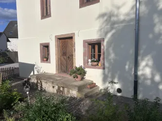 Ein charmantes Haus mit Holzfenstern und einer massiven Tür. Vor dem Haus befindet sich ein kleiner Garten mit Pflanzen.