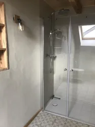 Eine moderne Dusche in einem hellen Badezimmer. Die Wände sind mit Putz versehen und es gibt ein großes Fenster über der Dusche.