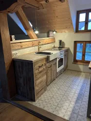 Eine moderne, gemütliche Küche mit Holzregalen und einem Fenster, das Licht hereinlässt. Die Einrichtung kombiniert traditionelle und funktionale Elemente.