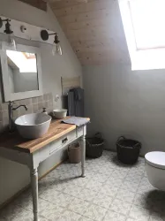 Ein modernes Badezimmer mit einem Waschbecken auf einem Holzschreibtisch. Die Wände sind hell und es gibt ein Dachfenster, das natürliches Licht hineinlässt.