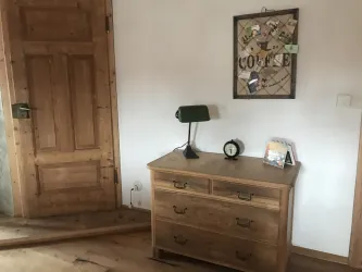 Ein Holzkommode mit einer Tischlampe und einer Uhr steht in einem Raum. An der Wand hängt ein Brett mit Notizen und Erinnerungen.