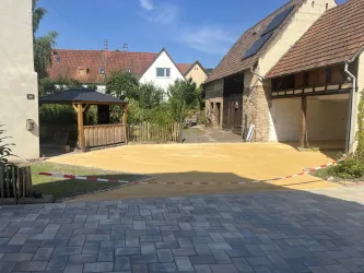 Ein Hof mit frisch aufgeschüttetem Sand und einer überdachten Sitzecke. Im Hintergrund sind mehrere Gebäude und ein klarer blauer Himmel zu sehen.