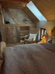 Ein gemütliches Schlafzimmer mit Holzdecke und rustikalem Mobiliar. Ein Platz zum Entspannen mit einem Sessel und sanfter Beleuchtung.