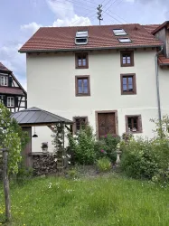 Ein gemütliches Haus mit einem roten Dach und mehreren Fenstern. Der Garten ist grün und blüht mit vielen Pflanzen.