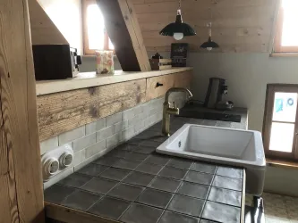 Eine gemütliche Küche mit Holzregalen und einem modernen Waschbecken. Die Fenster lassen viel Tageslicht herein und schaffen eine einladende Atmosphäre.