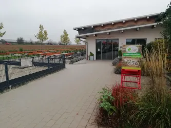 Ein modernes Gartencafé mit einem einladenden Eingang. Umgeben von pflanzlicher Vegetation und einem offenen Außenbereich.
