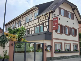 Ein charmantes Hotelgebäude im traditionellen Stil mit Fachwerk. Die Fassade ist freundlich und einladend, umgeben von Pflanzen.