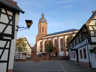 Ein malerischer Platz mit historischer Architektur und einer Kirche im Hintergrund. Die Gebäude haben hübsche Fachwerkmerkmale und der Himmel ist klar.