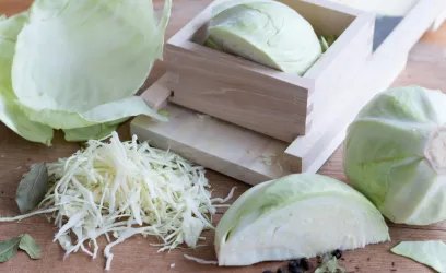 Ein frischer Kopf Weißkohl, in Stücke geschnitten und geraspelt. Daneben liegt eine Holzbox, die zur Aufbewahrung dient.