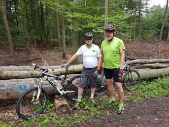 Zwei Männer stehen neben ihren Mountainbikes im Wald. Sie tragen Fahrradhelme und sportliche Kleidung.