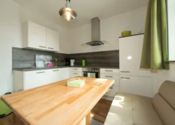 Eine moderne Küche mit hellen Schränken und Holzarbeitsplatte. Der Tisch in der Mitte ist mit einem kleinen grünen Objekt dekoriert.