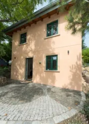 Ein schönes, helles Haus mit einem flachen Dach und grünen Fenstern. Der Eingangsbereich ist von einem runden, gepflasterten Weg umgeben.