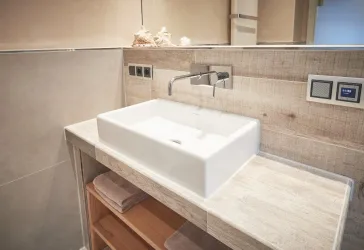 Ein modernes Badezimmer mit einem weißen Waschbecken und Holzregal. Die Wände sind in hellen, neutralen Farben gehalten.