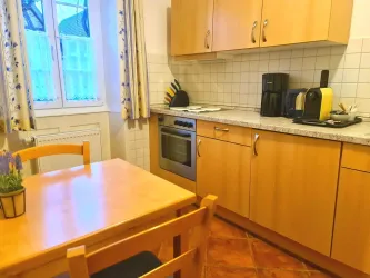 Eine gemütliche Küche mit hellen Holzschränken und modernen Geräten. Der Tisch und Stühle aus Holz stehen in der Ecke, neben einem Fenster mit Vorhängen.