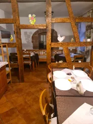 Ein gemütliches Restaurant mit Holzbalken und rustikaler Einrichtung. Tische sind mit weißen Tellern und Dekorationen gedeckt.