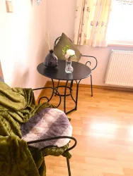 Ein gemütlicher Sitzbereich mit einem schwarzen Tisch und einer eleganten Vase. Eine grüne Decke liegt auf einem Stuhl und sorgt für eine einladende Atmosphäre.