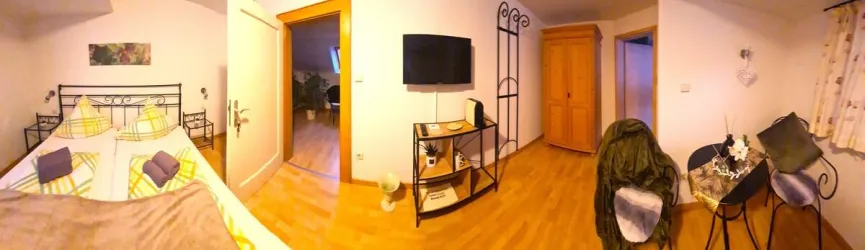 Ein gemütliches Zimmer mit einem Bett, Fernseher und einem kleinen Tisch. Die Wände sind hell und der Boden ist aus Holz.
