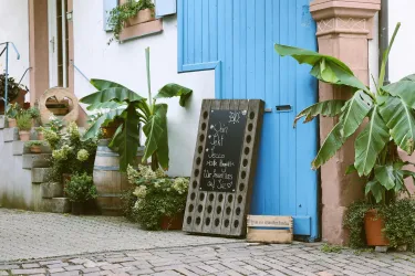 Ein schönes Café mit einer blauen Tür und einer Tafel im Freien. Banane und andere Pflanzen schmücken den Eingang.