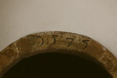 Ein steinerner Bogen mit der Jahreszahl 1575 in schwarzer Schrift. Der Hintergrund ist schlicht und hell.