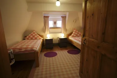 Ein gemütliches Zimmer mit zwei Einzelbetten und einem Holzschrank. Es gibt eine weiche Teppichfläche und angenehme Lichtquellen.