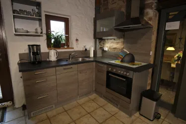 Eine moderne Küche mit Holzschränken und grauen Arbeitsflächen. Sie ist ausgestattet mit einem Herd, einer Kaffeemaschine und einem Waschbecken, umgeben von einem gemütlichen Ambiente.