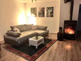 Ein gemütlicher Wohnraum mit einem grauen Sofa und einem kleinen weißen Tisch. Neben dem Sofa steht ein Kamin, der eine warme Atmosphäre schafft.