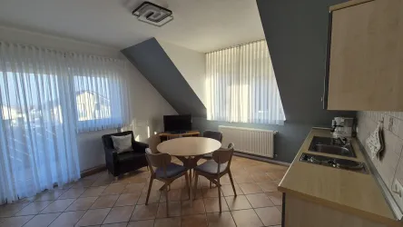 Eine helle Küche mit einem runden Tisch und Stühlen. Große Fenster lassen viel Licht hinein.