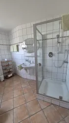 Ein sauberes Badezimmer mit einer Duschkabine und einem Waschbecken. Die Wände sind gefliest und es gibt Holzregale zur Aufbewahrung.