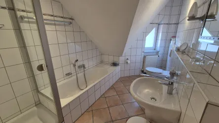 Ein modernes Badezimmer mit Fliesenboden und schrägen Wänden. Es ist ausgestattet mit einer Badewanne, Bidet, Dusche und Waschbecken.Föhn und Kosmetikspiegel vorhanden.