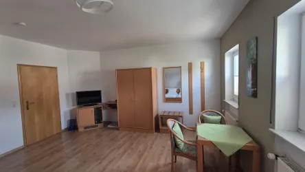 Ein gemütlicher Raum mit Holzfußboden und minimalistischer Einrichtung. Zu sehen sind ein Tisch mit zwei Stühlen und ein Fernseher in der Ecke.