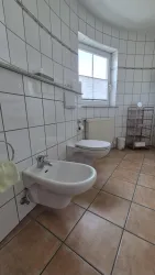 Ein minimalistisch eingerichtetes Badezimmer mit Fliesenboden. Es gibt ein Bidet, eine Toilette und einen Fensterblick.