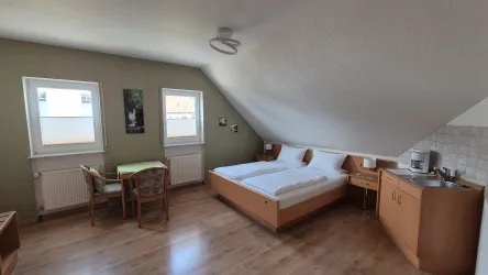 Ein helles Zimmer mit einem Doppelbett und Holzfußboden. Es gibt einen Tisch, Stühle und eine kleine Küchenzeile.